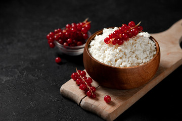 fresh home-made cottage cheese with currants in a wooden bowl against a dark background, healthy food with berries on a black table