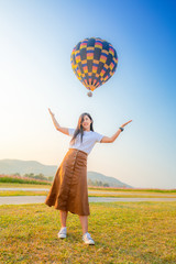 A woman standing on the green grass and happily take a picture with a hot air balloon