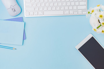 Flat lay blogger or freelancer workspace with a keyboard, flowers in a vase, office supplies on a color background