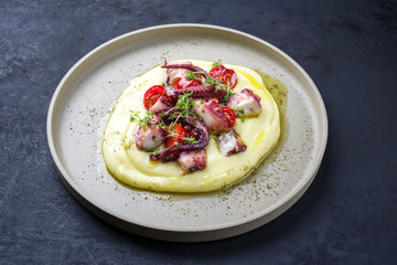 Traditional Italian polpo alla griglia su crema di patate with barbecued octopus, potato creme and tomatoes as closeup on a modern design plate