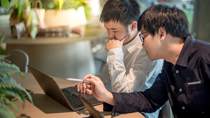 Business meeting and partnership concept. Asian man colleagues discussing about startup project using laptop computer and digital tablet in office. Coworkers team sharing ideas together at workplace.