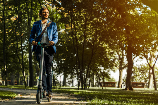 Young Handsome Business Man Riding On Electric Scooter Through Park In Office