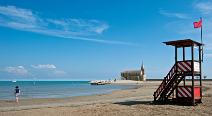 Fototapeta na wymiar Girl on the beach of Caorle, a beautiful seaside resort in the Veneto, in the background the church of Madonna dell'Angelo. Italy