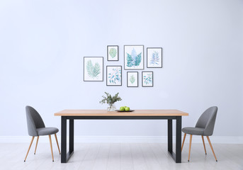 Stylish room interior with modern table, chairs and paintings of tropical leaves. Idea for design