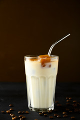 Transparent glass with milk and ice cubes made from coffee. Iced coffee with a metal tube on a dark brown background. Vertical orientation with copy space.