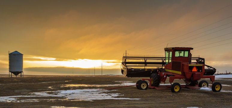 Farm combine sitting in an empty field amongst the setting sun