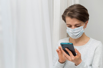 A woman in a medical protective mask uses a mobile phone, writes a message.