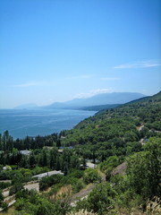 Naklejka premium Sea view from the coastal mountains. The coastal hills are surrounded by dense vegetation, including low buildings. In the distance, on the horizon, you can see the coastal mountains in the haze.
