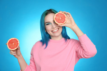 Young woman with bright dyed hair holding grapefruit on light blue background