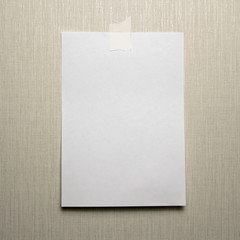 A4 white sheet of paper hanging on a wall glued with a piece of paper tape on a light background.