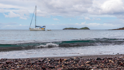 Plage de galets et sable noir, voilier et ilets sur la mer des caraibes