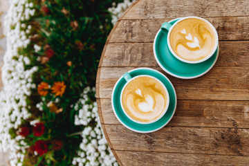 Freshly brewed coffee with heart shape on top placed in two light blue cups on saucers. Hot morning drinks served for couple on wooden table.