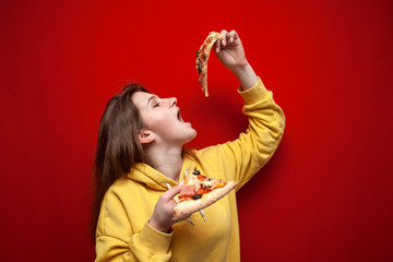 young happy girl eating pizza on a colored background, a teenager holds two slices of pizza and eat...
