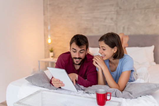 Couple drinking coffee and using tablet computer in bed