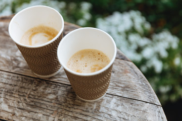Close up of wooden round table with couple of paper brown cups of fresh hot coffee with blur background. Wake up and drinks coffee concept.