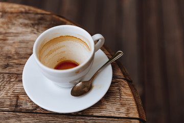 Empty hot coffee in white ceramic cup with dirty spoon after drink on wooden table with copy space. Aftertaste of aroma cappuccino in coffee shop