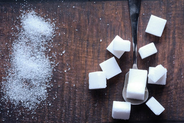 top view of sugar cube on spoon on wooden background 