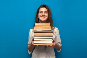 young beautiful funny girl the nurse holds many books on a blue background and is smiling, the student is studying in a medical college