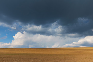 Freshly plowed land and ovescast blue sky with storm clouds