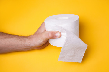 Male hand holds toilet paper on a yellow background. Coronavirus concept. Stay at home