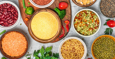 Various cereals and legumes. Beans, peas, lentils, mung bean, polenta and bulgur in bowls on a gray concrete background, top view. Protein foods for vegans and vegetarians.