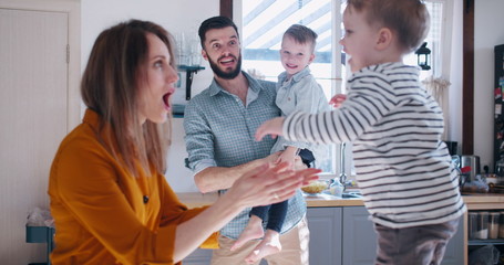 Happy young Caucasian mother and father playing with two little sons in the kitchen, family fun...