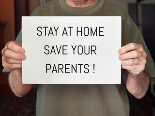the hands of an old man hold a white sheet with the text stay at home, save your parents. coronavirus, covid-19.