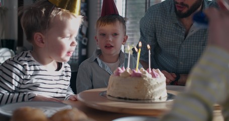 Cute happy little Caucasian boy child making wish, blowing on birthday cake at fun celebration with family slow motion.