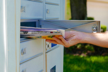 A hand is pulling a pile of mail out of a mailbox - obrazy, fototapety, plakaty