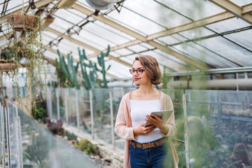 Woman researcher standing in greenhouse, using tablet.