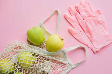 Safe shopping in quarantine concept. Pink gloves and tote bag with fresh apples on pink background flat lay. Stay safe. Prevention of virus epidemic. Order food online with delivery and stay home