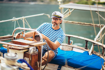 Mature man standing at helm of sailboat out at sea on a sunny afternoon.