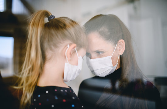 Mother and child with face masks indoors at home, Corona virus and quarantine concept.