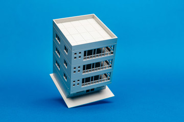 Model of a building balancing on one edge on a blue background