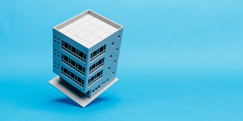 Model of a building balancing on one edge on a light blue background