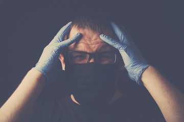 A young man in a black mask and medical gloves on a black background shot in a low, dark key,...