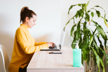 young woman working on laptop at home, using hand sanitizer alcohol gel. Stay home during coronavirus covid-2019 concept