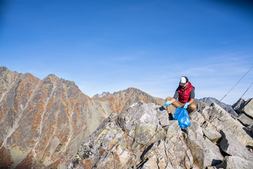 Man hiker picking up litter in nature in mountains, plogging concept.