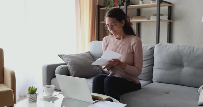 Happy excited woman reads good news in mail letter sits on sofa at home. Overjoyed lady winner holds bank paper receiving approved loan, tax refund or salary notice, celebrating success concept.