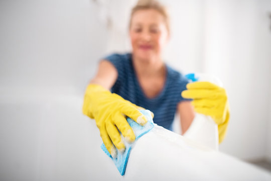 Senior woman with gloves cleaning bathroom indoors at home.