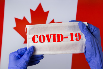Coronavirus outbreak. Coronavirus update in Canada. Word Covid-19 on medical mask with flag of Canada on background. Spread of corona virus in world. Wuhan virus.