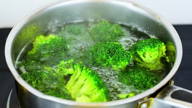Cooking organic broccoli florets in small stainless steel saucepan.Vegan meal preparation.Healthy eating.One of five a day.Close up footage of  green vegetable in pan with boiling water with steam. 
