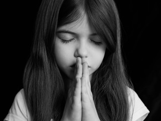 young girl prays, portrait on a dark background, black and white photo