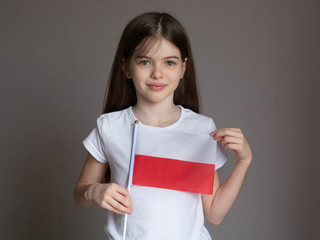 Little / young girl with long hair in a white T-shirt holds the Polish flag. Language school concept. Learning Polish. Immigration to Poland