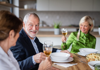 Group of senior friends at dinner party at home, with glasses of wine.