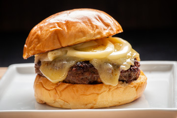 Cheeseburger pão com queijo e requeijão derretido em prato quadrado com fundo escuro 