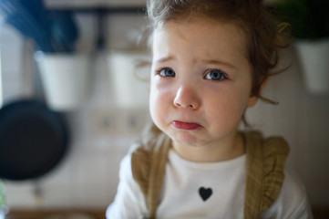Small sick toddler girl indoors at home, looking at camera.