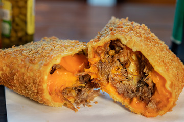 Pastel frito da culinária brasileira de massa crispy com recheio de costela com cheddar encima de guardanapo  com fundo de pimenta 