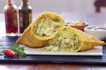 Pastel da culinária brasileira de bacalhau com ervas finas com pimenta e molho ao fundo 