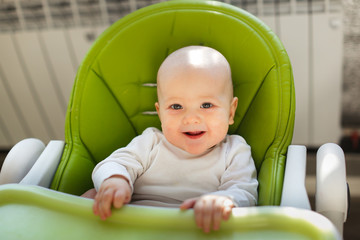 bald Caucasian baby happy in green child chair